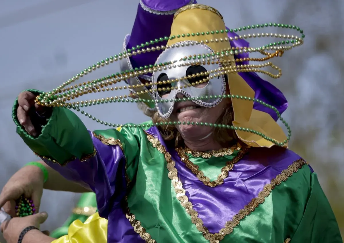 Masked reveler in a purple, green, and gold satin costume throwing strands of beads